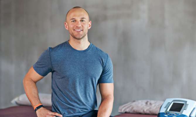 Man in a gym, smiling, sitting beside medical equipment.