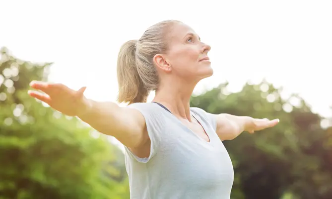 Woman stretching arms outside, looking upward, in a green park.