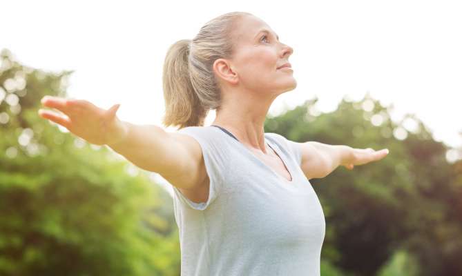 Woman stretching arms outside, looking upward, in a green park.
