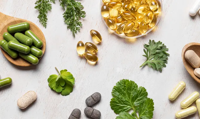 Herbal supplements and capsules on a light surface with green leaves.