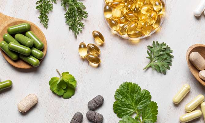 Herbal supplements and capsules on a light surface with green leaves.