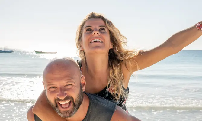 Smiling couple piggybacking on a sunny beach day.