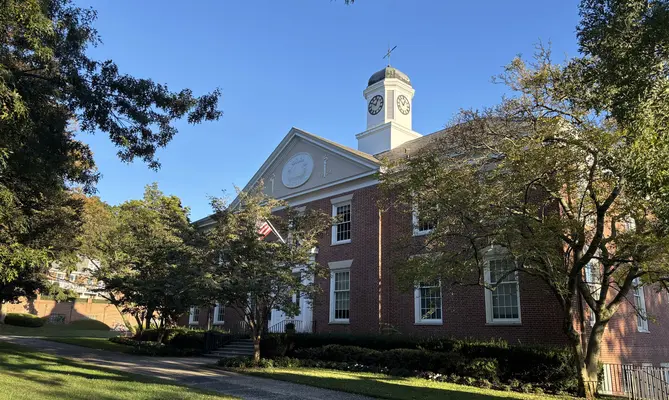 Red brick building with a clock tower, trees, and blue sky in Ladue, MO.