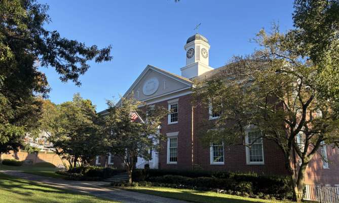 Red brick building with a clock tower, trees, and blue sky in Ladue, MO.