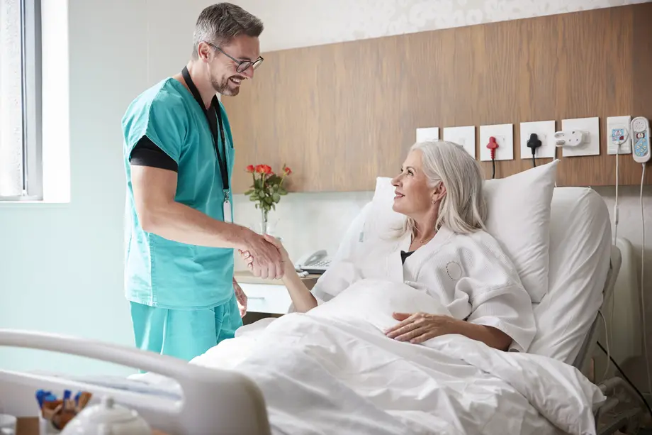 Doctor shaking hands with smiling patient in hospital bed.