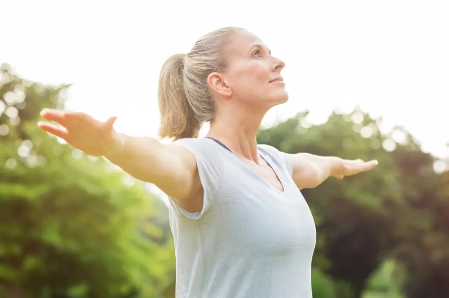 Woman stretching arms outside, looking upward, in a green park.