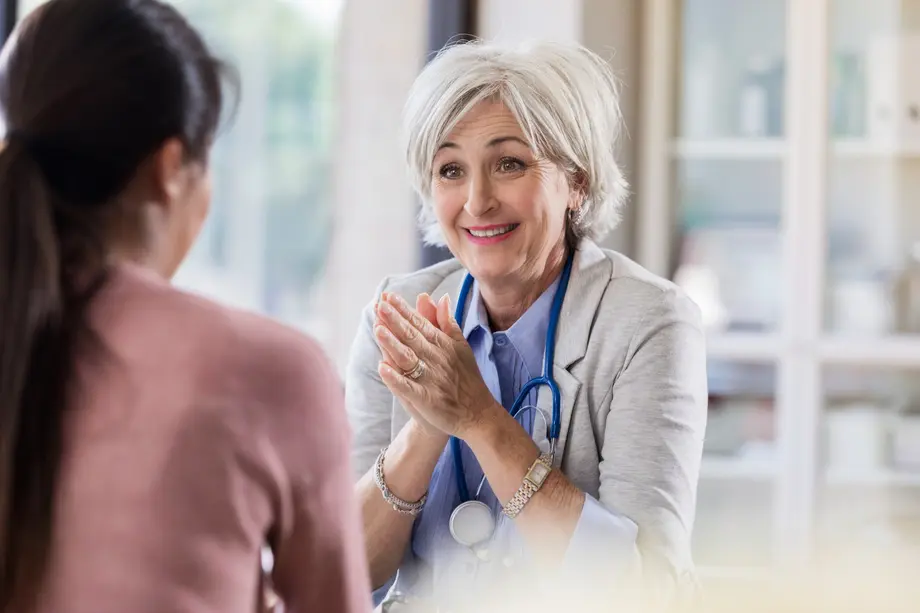 Smiling doctor in office speaks with patient, stethoscope around neck.