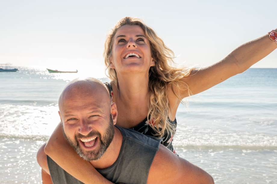 Smiling couple piggybacking on a sunny beach day.