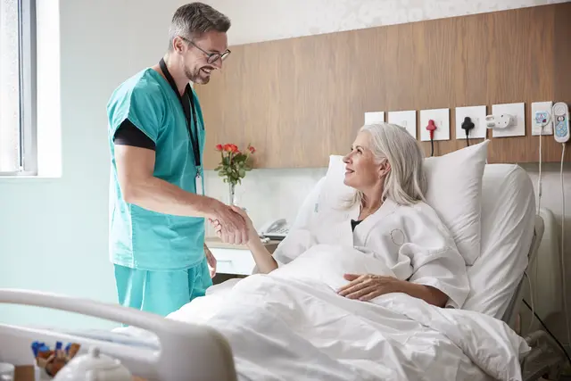 Doctor shaking hands with smiling patient in hospital bed.