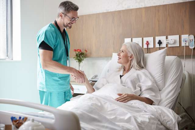 Doctor shaking hands with smiling patient in hospital bed.