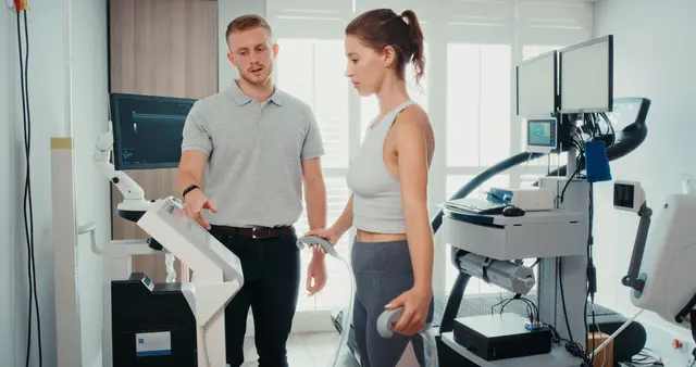 Woman in activewear using medical equipment with a technician in a clinic.