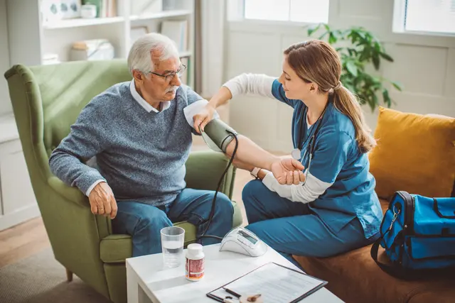 Nurse checking an elderly man's blood pressure at home.