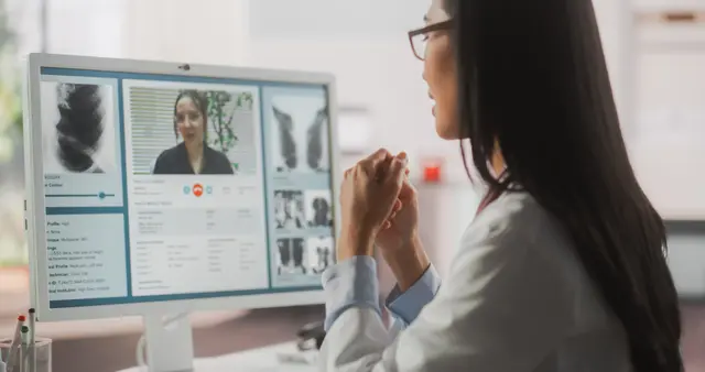 Doctor in video call with patient on computer monitor.