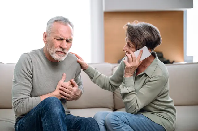 Man clutching chest, woman on phone, looking concerned.
