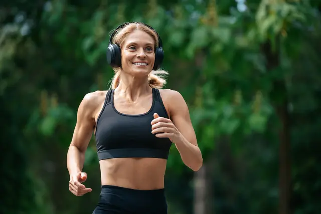 Woman jogging in a park, wearing headphones and a black sports bra.