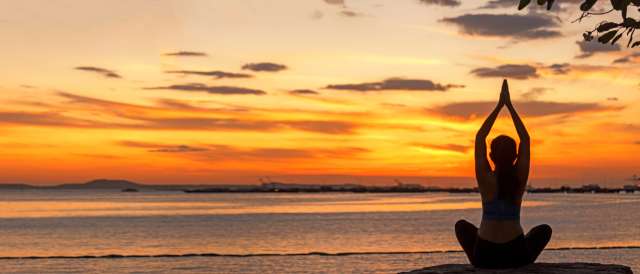 Person doing yoga at sunset by the ocean.