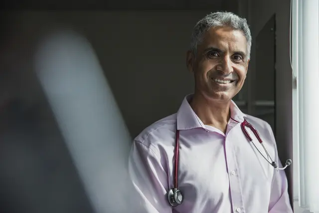 Smiling doctor with stethoscope in a light-filled room.