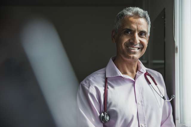 Smiling doctor with stethoscope in a light-filled room.