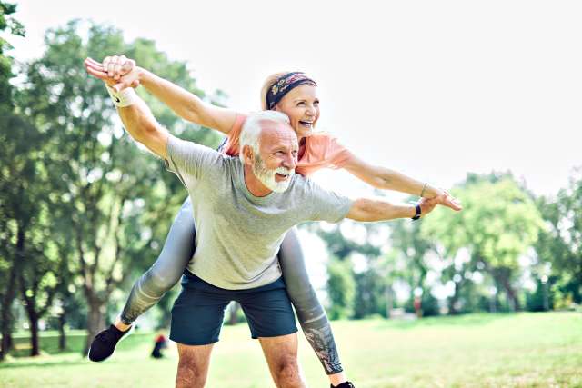 Elderly couple playing in a park, man gives woman a piggyback ride.