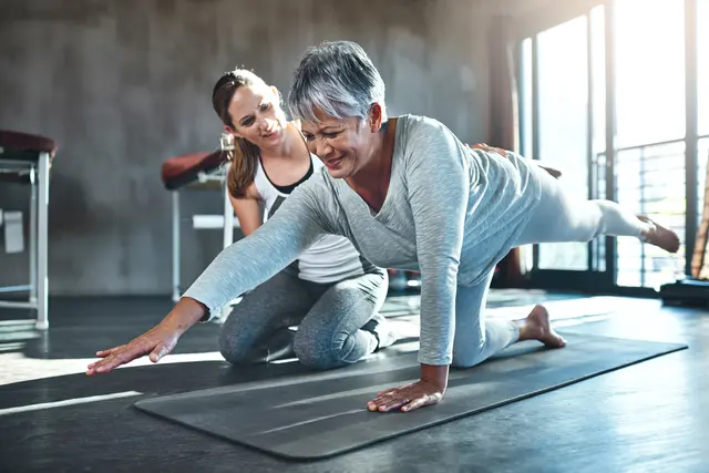 Woman doing yoga stretch with instructor guiding her.