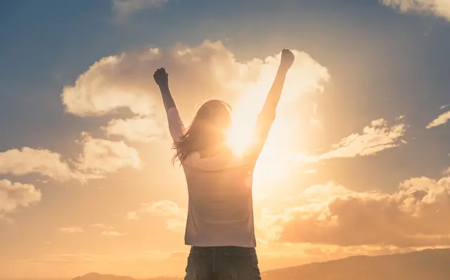 Person celebrates with raised arms at sunset.