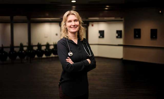 Dr. Kathryn Shoemaker, MD, smiling, with stethoscope in a hallway, arms crossed.