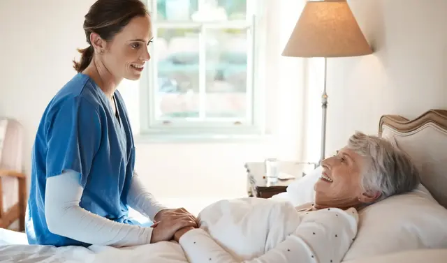 Nurse smiling at an elderly woman in bed.