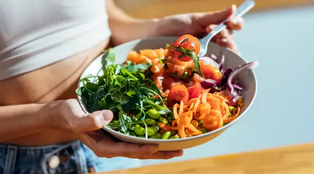 Person holding a colorful salad with greens and vegetables.