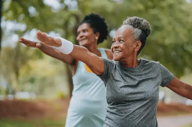 Two women enjoying outdoor yoga, smiling with arms outstretched.